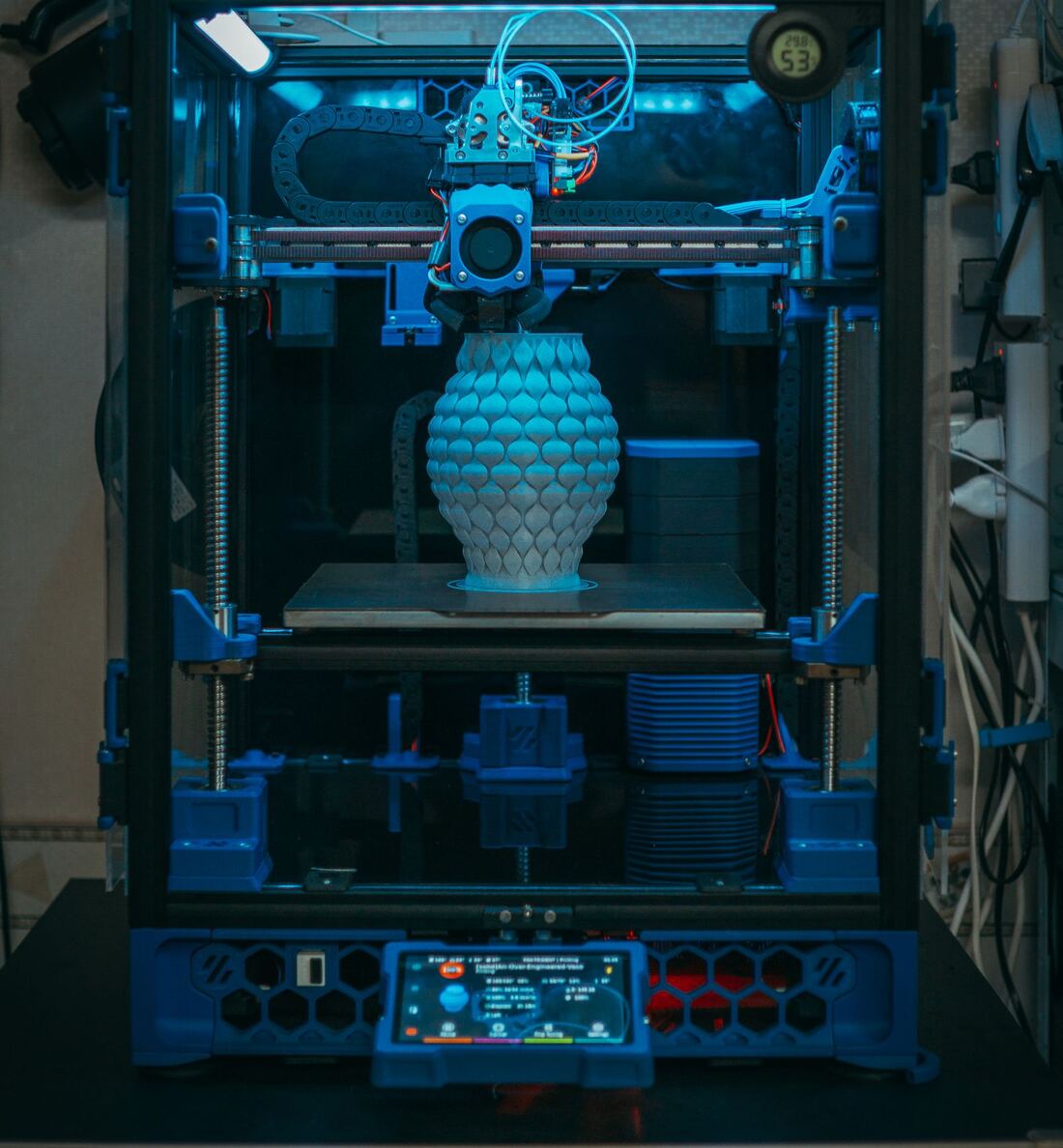 Enclosed 3D printer lit blue, printing a textured vase