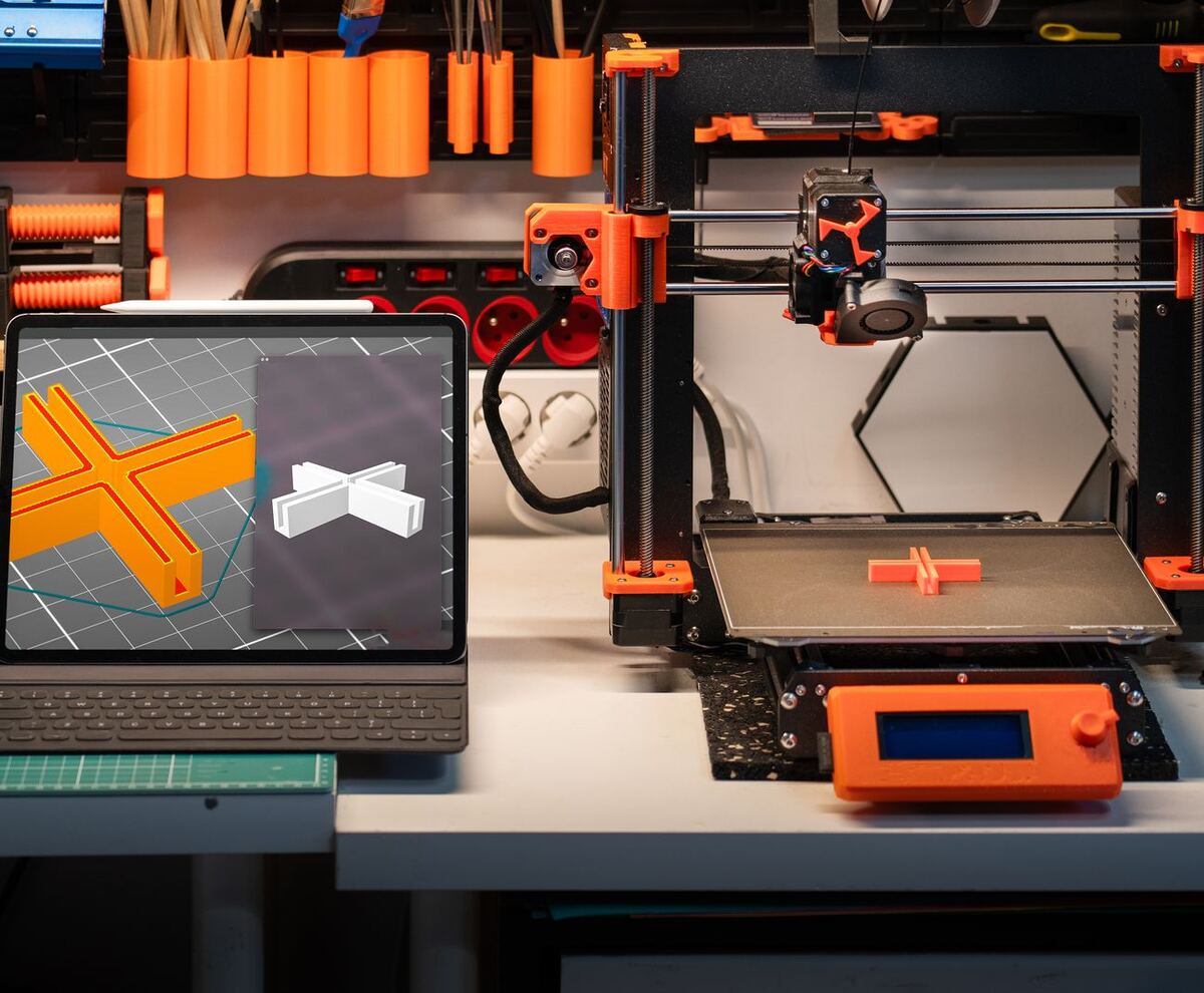 Laptop showing a 3D model in a slicer beside a 3D printer