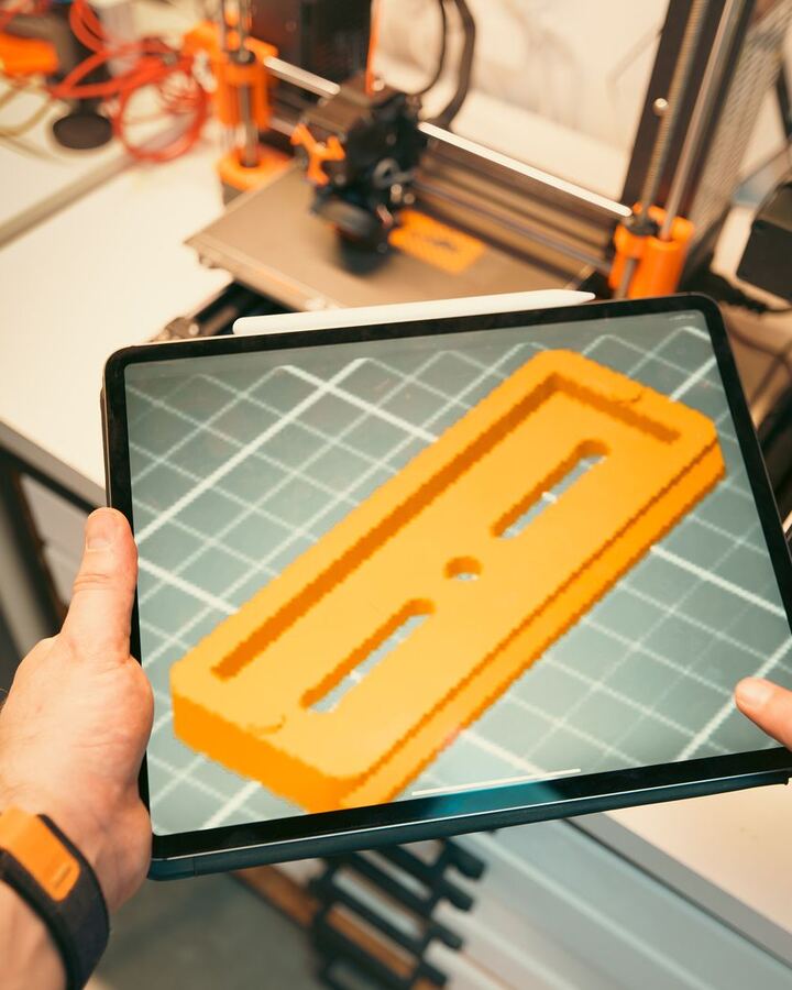 Hands holding a tablet showing a 3D part in a slicer